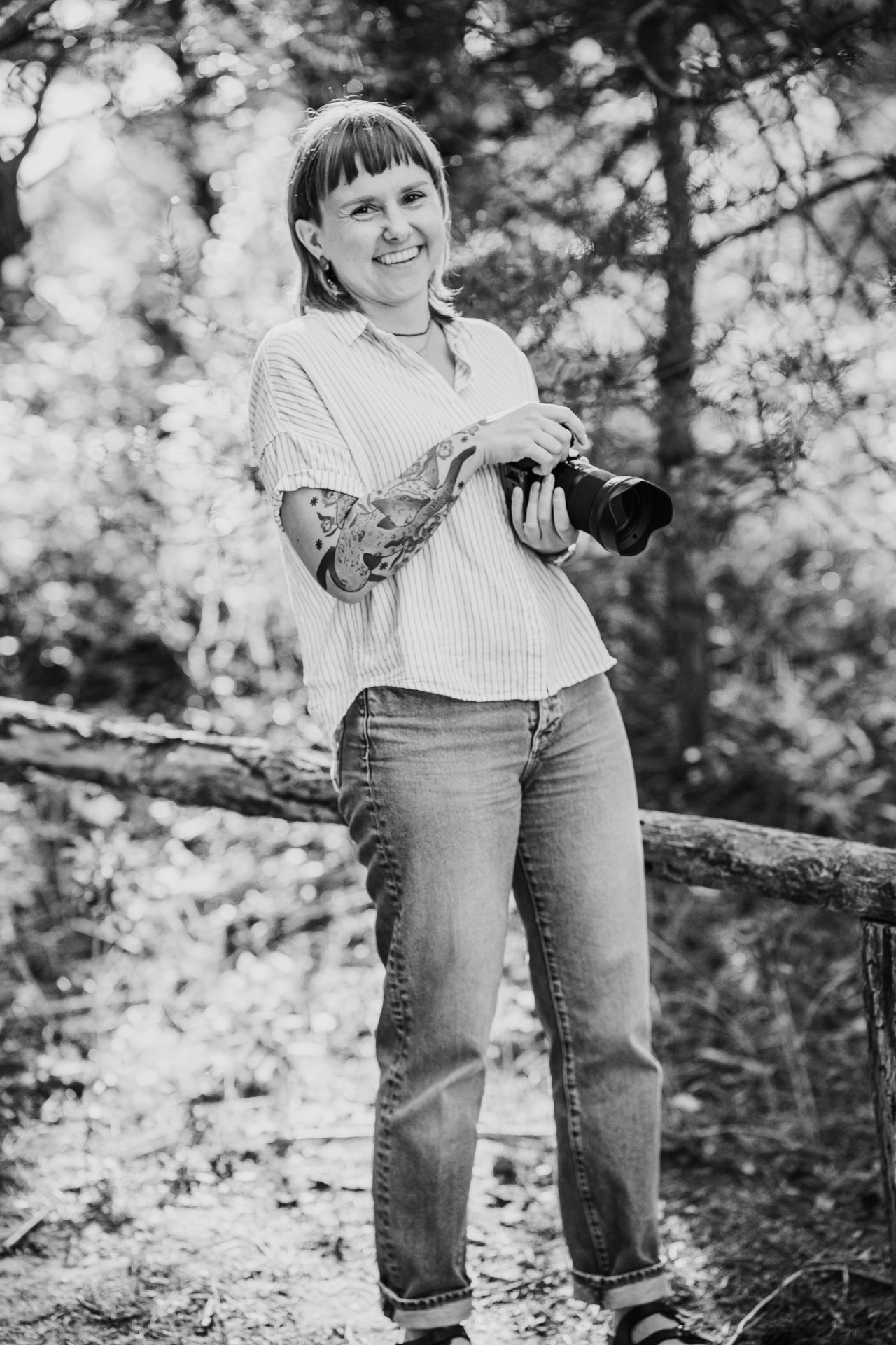 Junge Hochzeitsfotografin Frau Eska in der Natur: Mit Kamera in der Hand und Blick in die Kamera