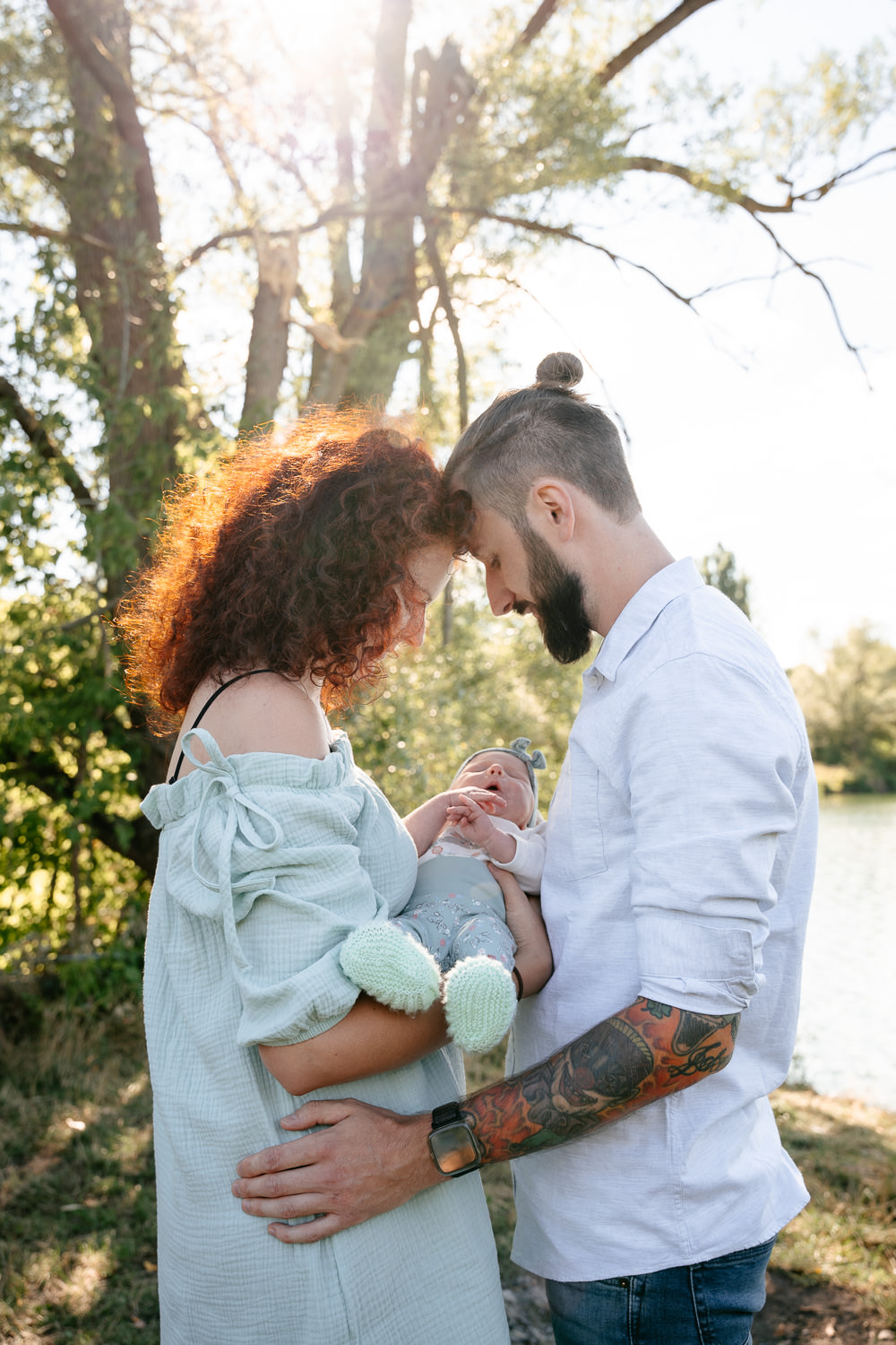 Familienshooting: Mama und Papa stehen zueinander und halten ihr Baby liebevoll im Arm