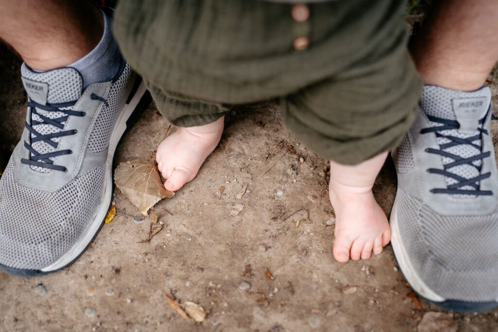 Familienshooting Outdoor: Kleine Babyfüße stehen neben den großen Füßen des Papas – innige Vater-Kind-Momentaufnahme
