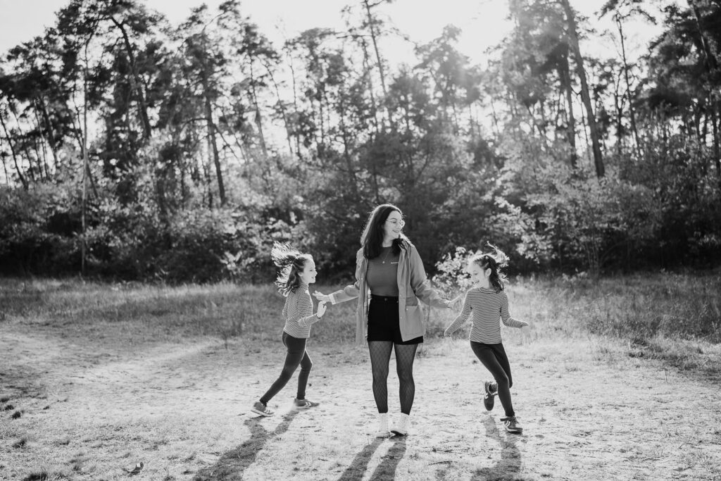 Familien Fotoshooting: Mama tanzt mit ihren zwei Töchtern im goldenen Sonnenlicht – fröhliches Familienshooting Outdoor