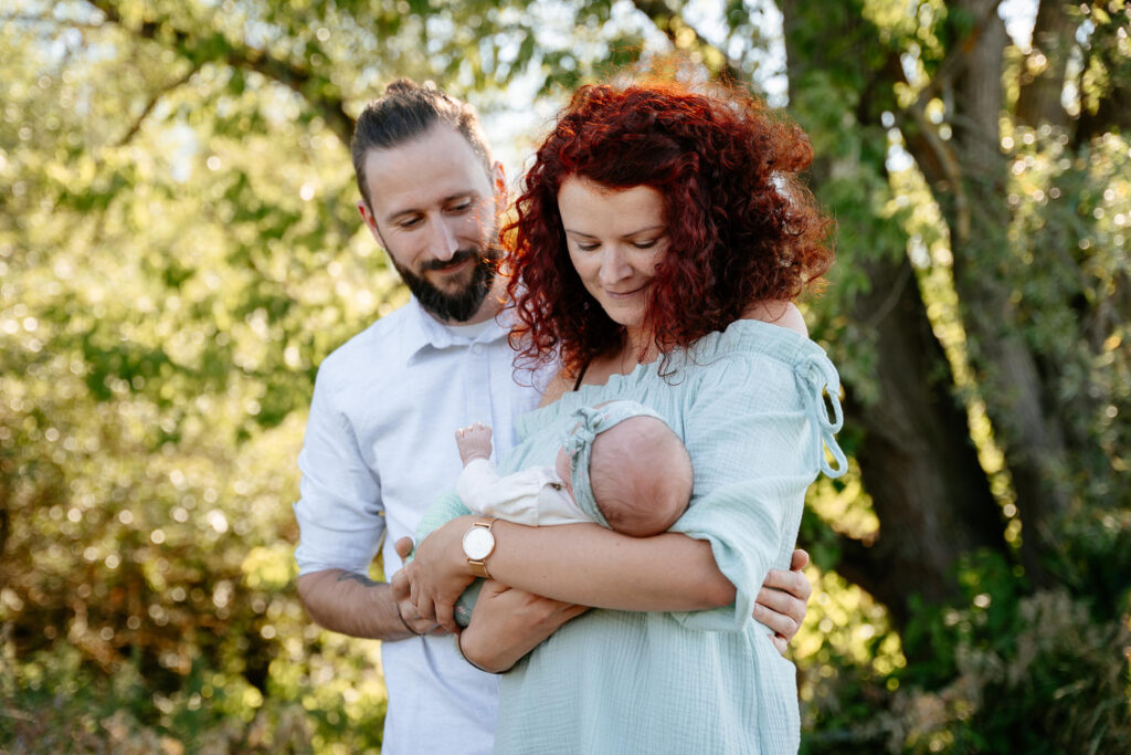 Familienfoto in der Natur: Eltern halten ihr Baby liebevoll im Arm und betrachten es