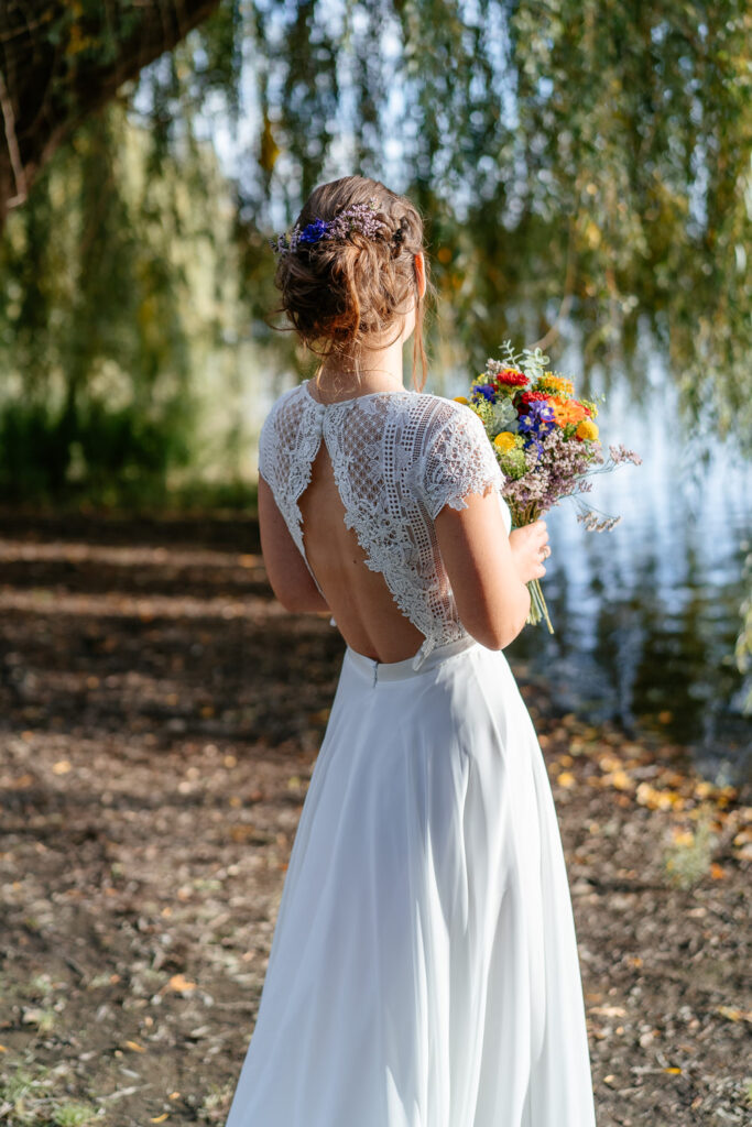 Brautpaar-Shooting Outdoor: Braut von hinten mit wunderschönem Rückenausschnitt im Brautkleid
