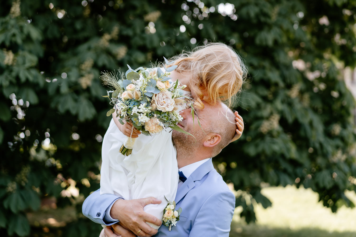 Emotionales Hochzeitsfoto: Bräutigam hält seine Tochter im Arm, während sie ihm einen Kuss auf den Kopf gibt