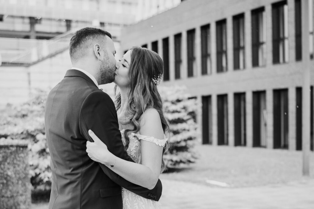 Hochzeitsfoto in Schwarz Weiß: Brautpaar küsst sich im Freien beim First Look