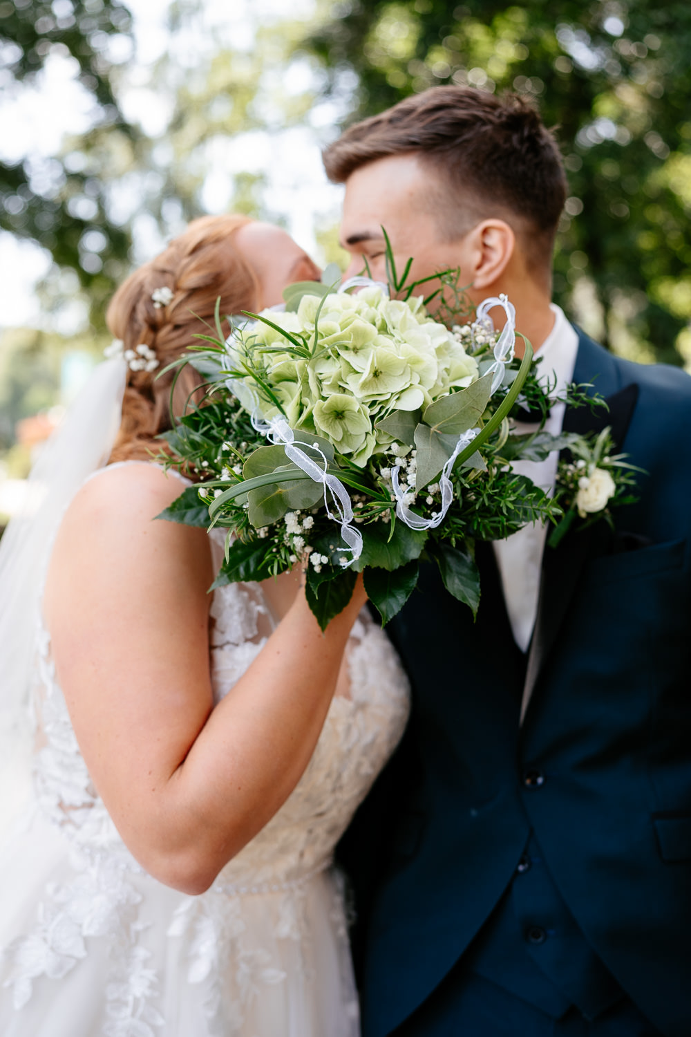 Hochzeitsfotos: Hochzeitspaar küsst sich romantisch hinter dem Brautstrauß
