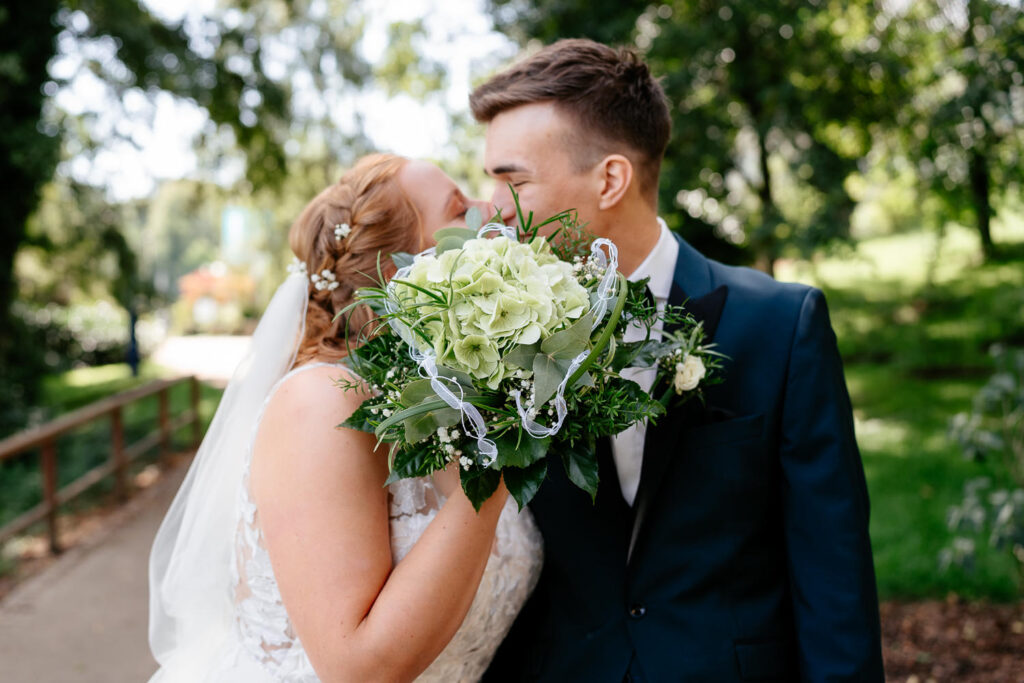 Hochzeitsfotos: Hochzeitspaar küsst sich romantisch hinter dem Brautstrauß