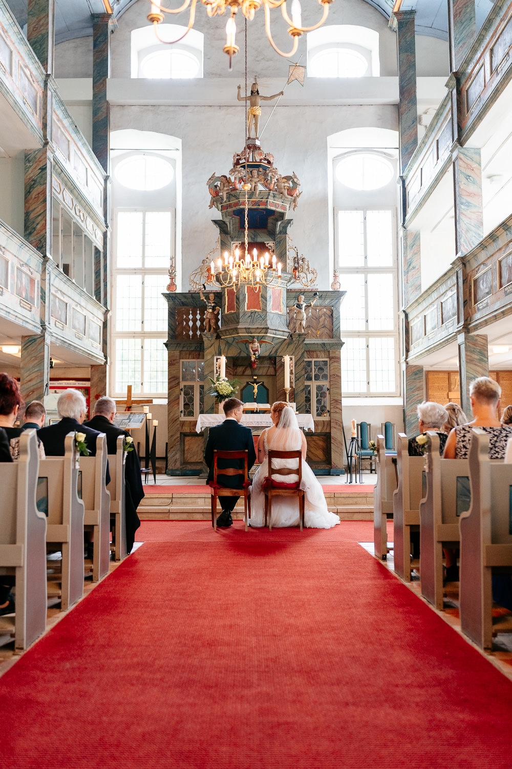 Hochzeitsbilder: Brautpaar sitzt bei der Trauung auf zwei Stühlen vor dem Altar in der Kirche