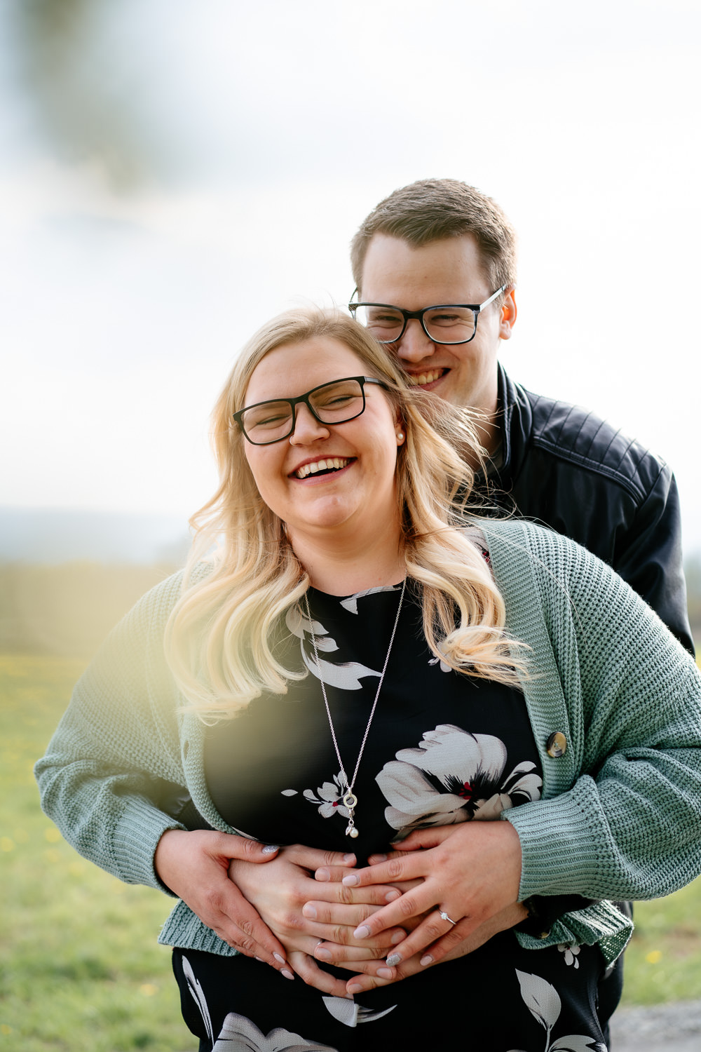 Paar Fotoshooting Outdoor: Er steht hinter ihr, beide lachen herzlich