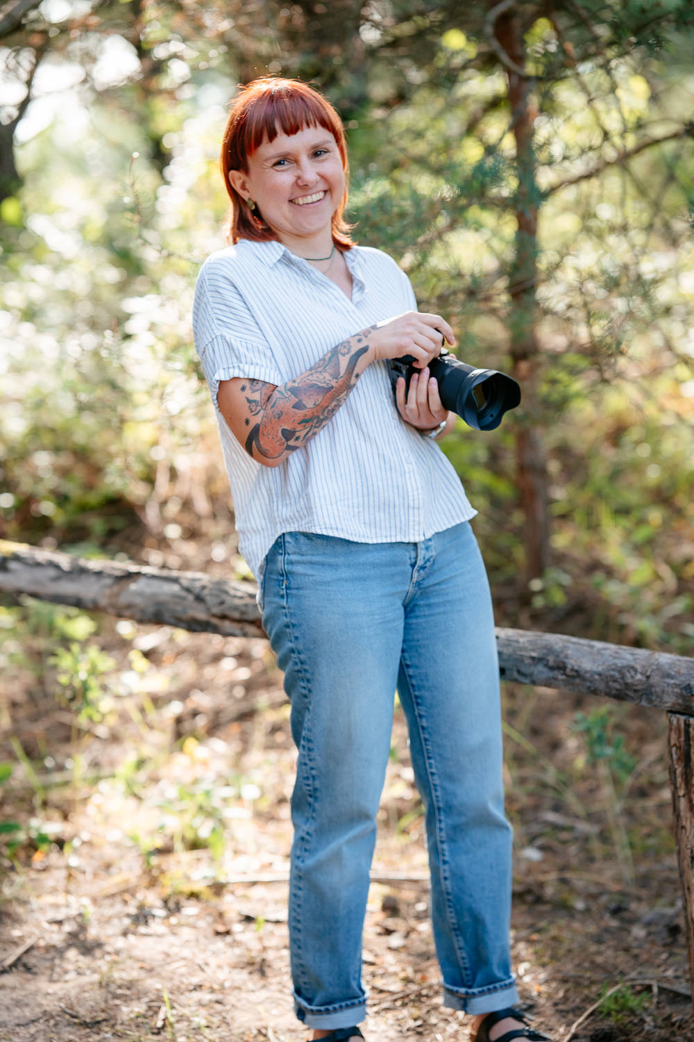 Junge Hochzeitsfotografin Frau Eska in der Natur: Mit Kamera in der Hand und Blick in die Kamera